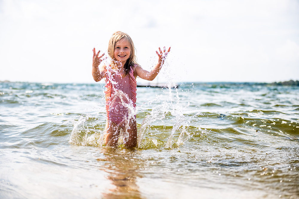 Flicka i randig baddräkt som badar på stranden i Karlskrona kommun